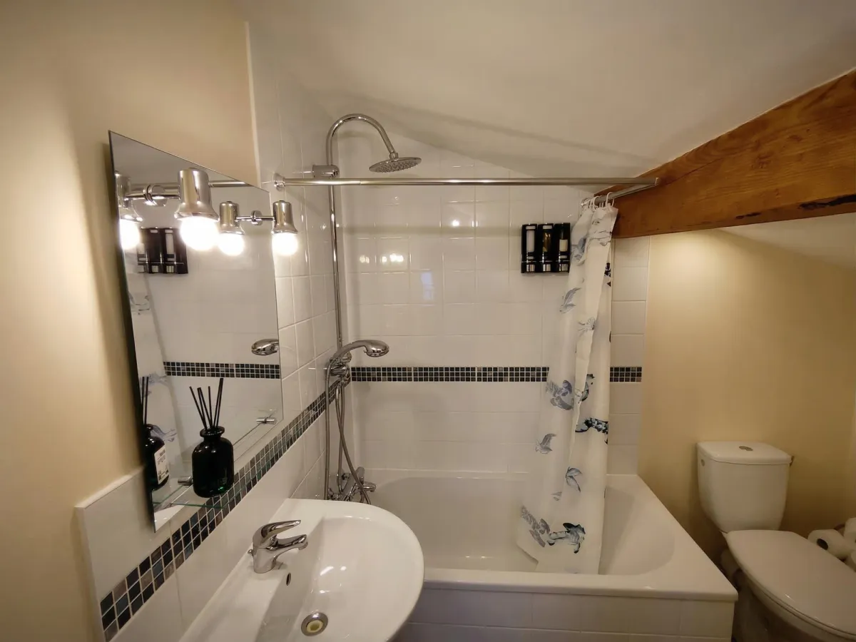Salle de bain avec baignoire, douche, carrelage blanc et plafond incliné