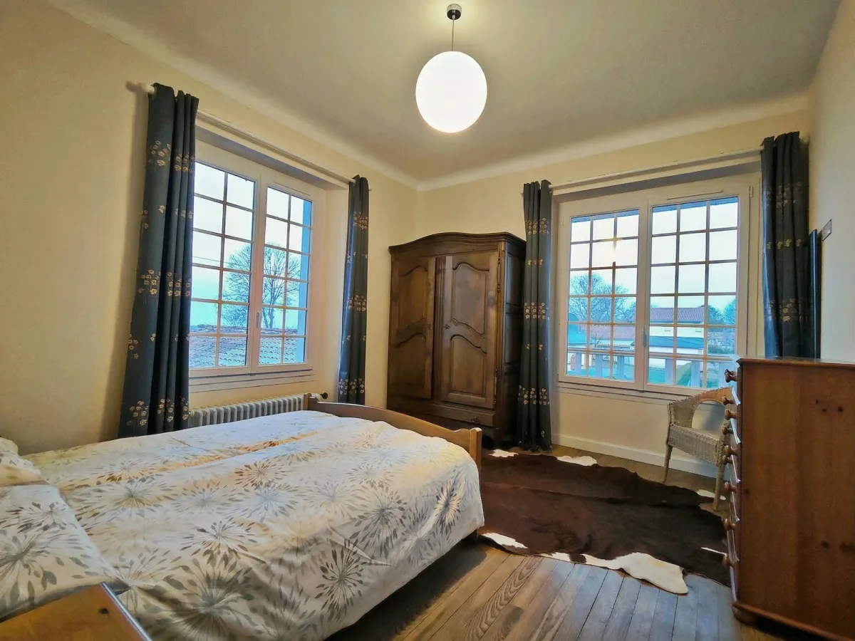 Chambre avec deux grandes fenêtres, armoire en bois et lit en bois