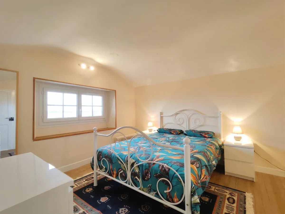 Chambre mansardée avec lit en métal blanc et petite fenêtre basse