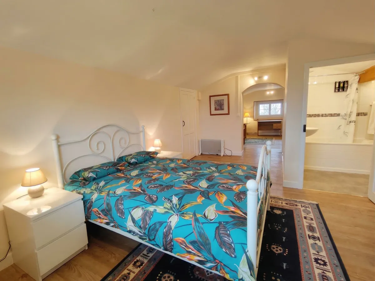 Chambre mansardée avec lit blanc, couvre-lit bleu et vue vers la salle de bain