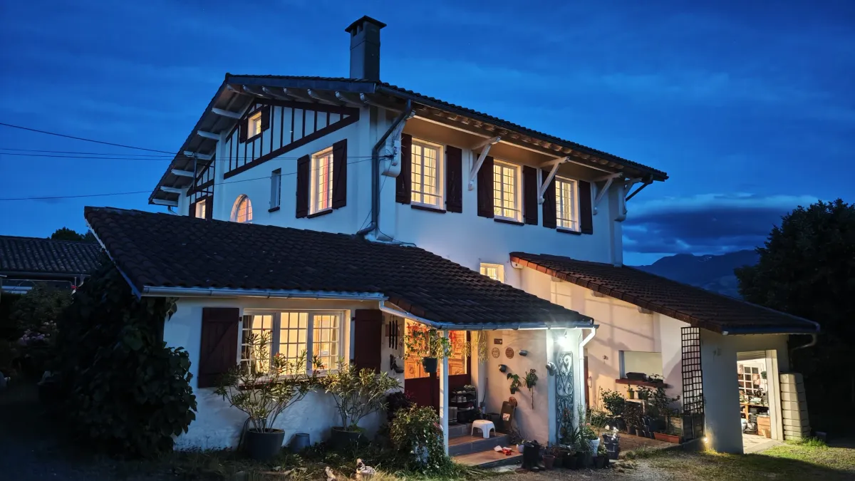Façade de HI PYRENEES à l'heure bleue, avec l'entrée éclairée sous un ciel du soir