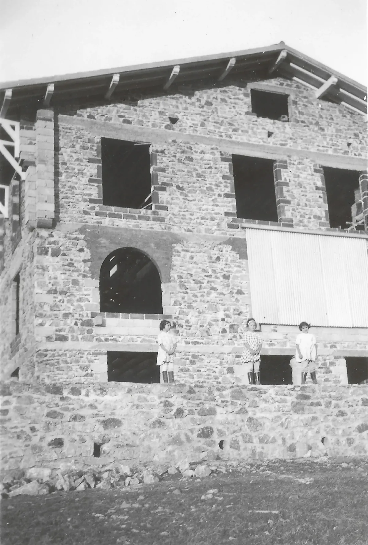 Ancienne photo de trois jeunes filles devant la façade en pierre de la maison